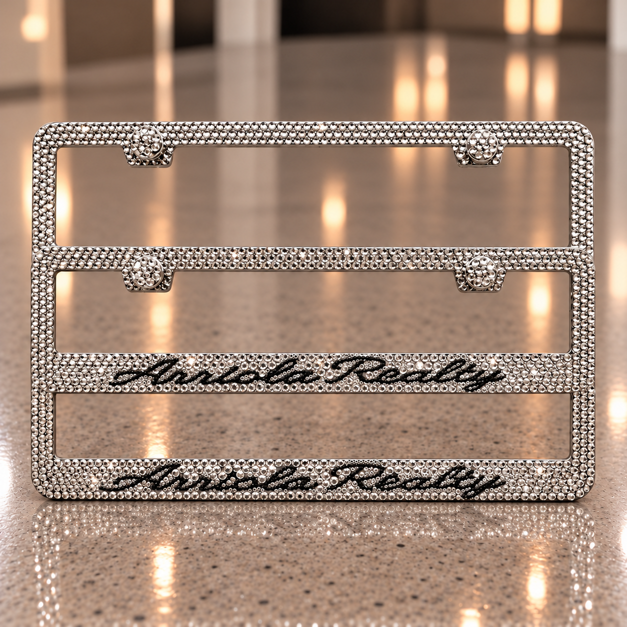 Two rhinestone license plate frames with Areola Realty in black script on a warm taupe stone background