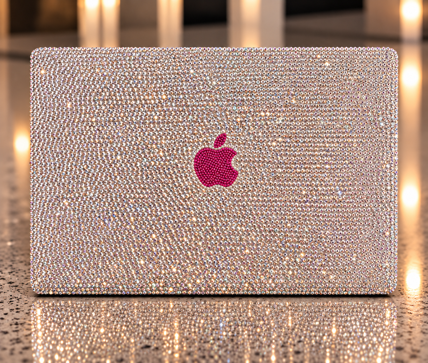 Rhinestone-covered MacBook with a pink Apple logo on a warm reflective surface