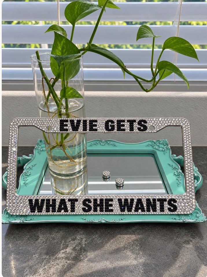 Rhinestone license plate frame with EVIE GETS and WHAT SHE WANTS lettering on a vanity tray