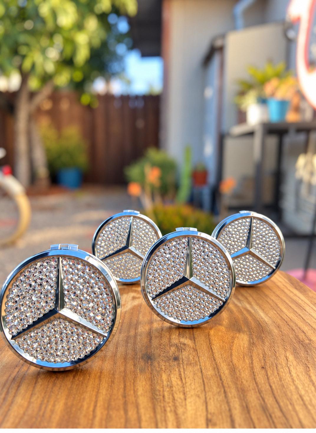 Four crystal Mercedes-Benz center caps displayed on a wooden tabletop