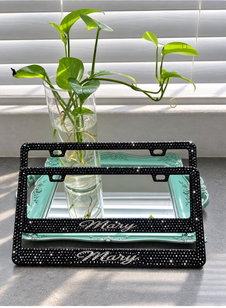 Two personalized black rhinestone license plate frames displayed on a vanity tray