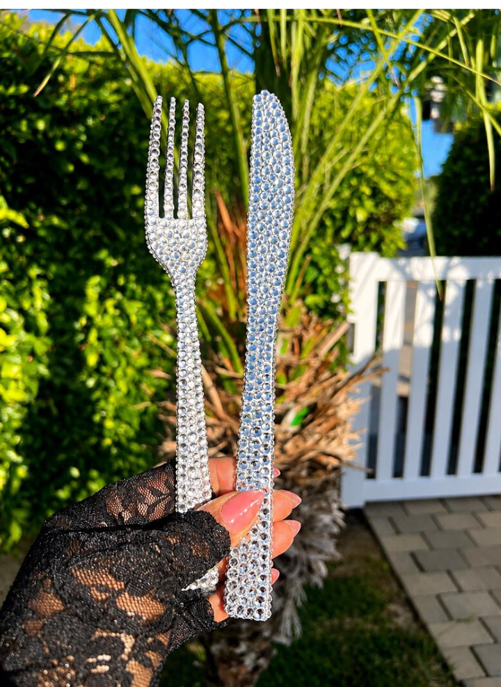 Rhinestone-covered fork and knife held in a garden setting