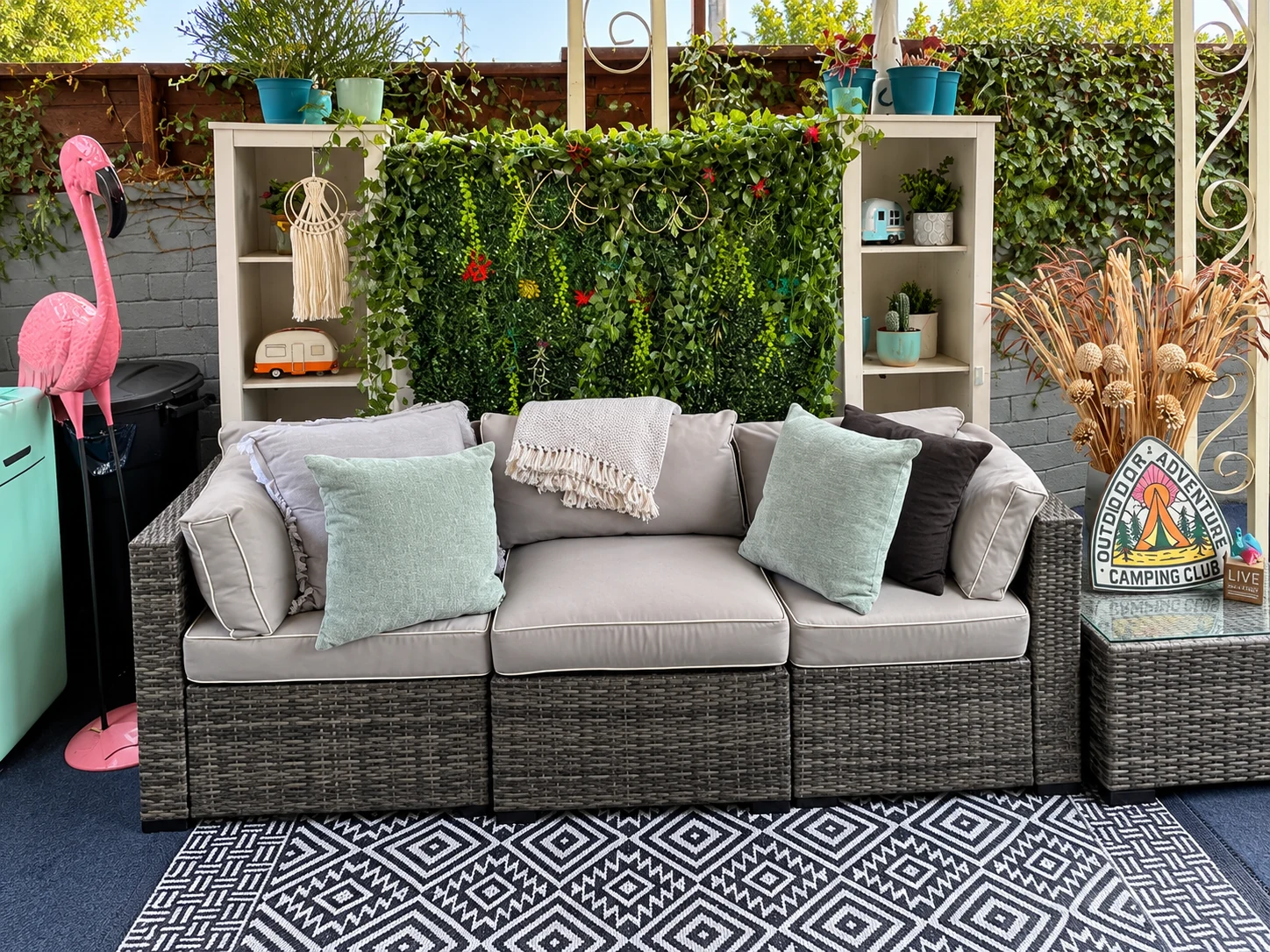 The patio lounge with a sofa, woven seating, and a leafy wall